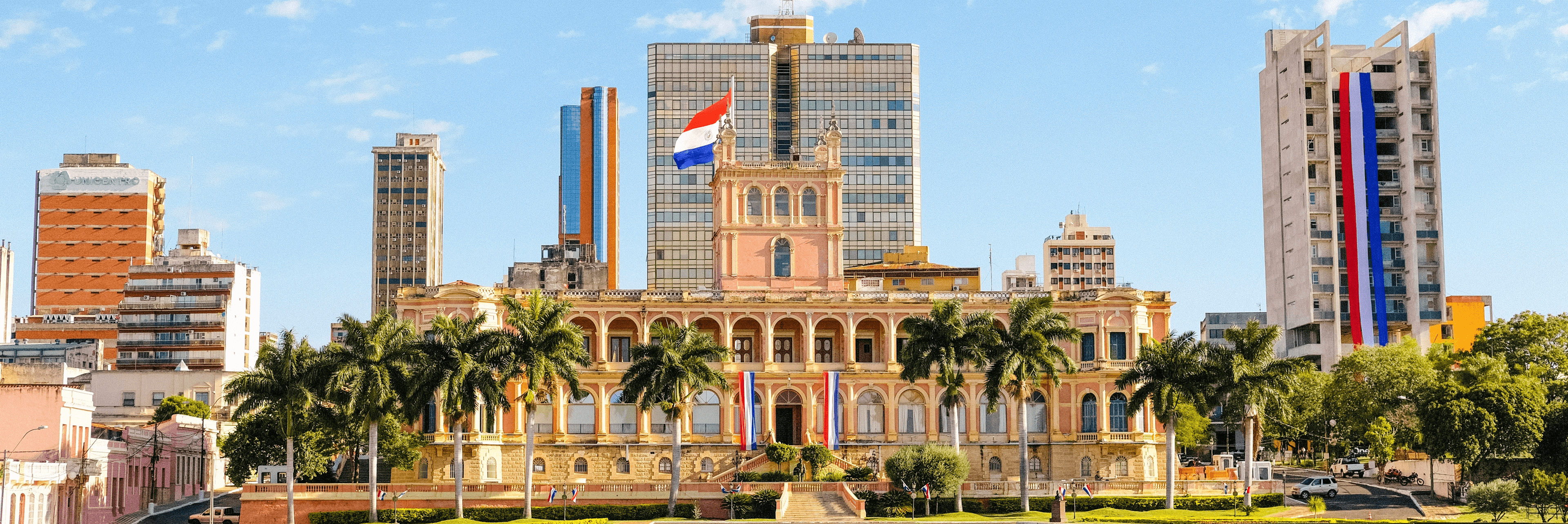 The Palacio de los López, Paraguay's presidential palace, decorated with Paraguayan flags and framed by palm trees and the Asunción city skyline